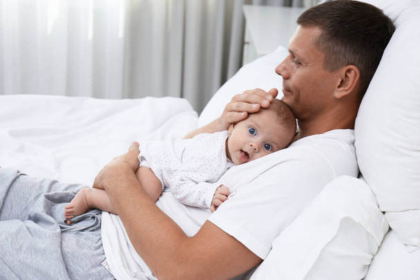 Happy father holding his cute baby on bed at home - Zdjęcie, obraz