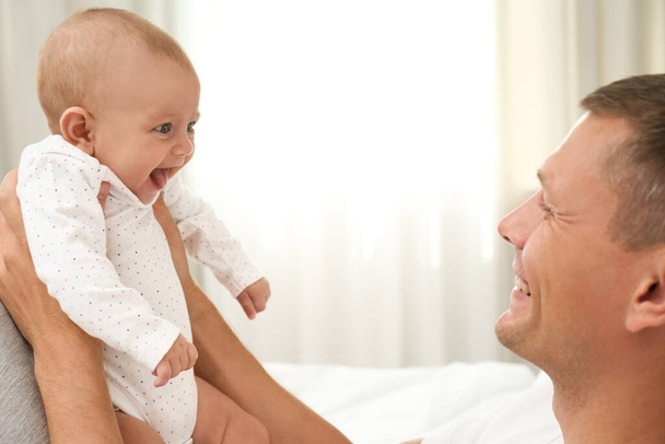 Happy father holding his cute baby on bed at home - Φωτογραφία, εικόνα