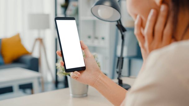 Fiatal ázsiai hölgy használja okostelefon üres fehér képernyő mock up kijelző reklám szöveg, míg az okos dolgozik otthonról a nappaliban. Chroma kulcs technológia, Marketing design koncepció. - Fotó, kép