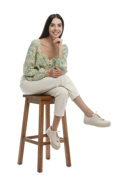 Beautiful young woman sitting on stool against white background - Photo, image