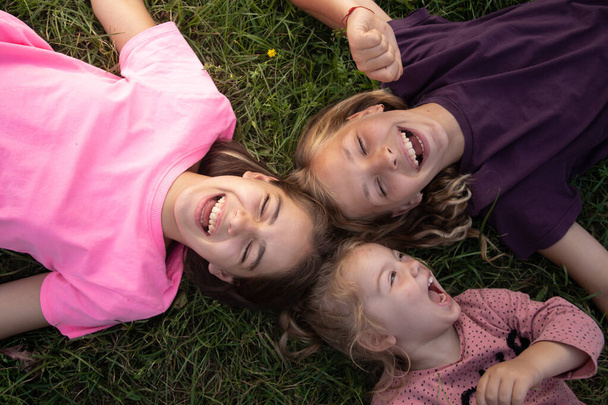Widok z góry na trzy dziewczyny śmiejące się leżące na trawie na zewnątrz. Beztroski szczęśliwy koncepcja dzieciństwa - Zdjęcie, obraz