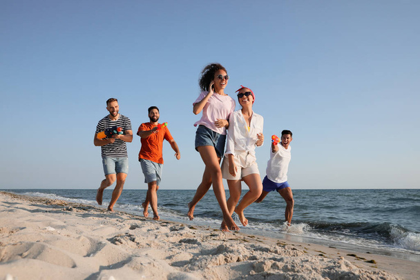 Group of friends with water guns having fun on beach - Valokuva, kuva