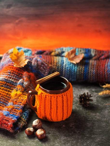 herfst compositie met warme herfst koffie of thee in een kopje met een gebreide oranje trui, oranje achtergrondverlichting - Foto, afbeelding