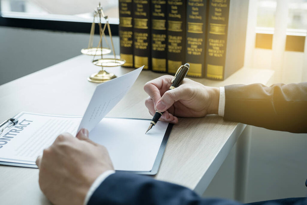 Advocaat hand holding pen en het verstrekken van juridisch advies zakelijke geschillenbeslechting op kantoor met schaal justitie en hamer hamer. - Foto, afbeelding