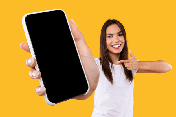 Woman showing white empty smartphone screen and pointing - Valokuva, kuva