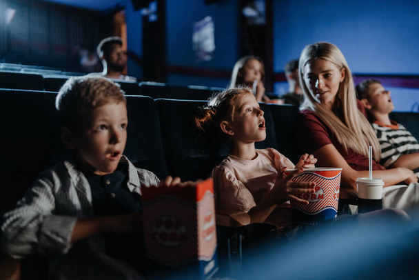 Mother with happy small children in the cinema, watching film. - Valokuva, kuva