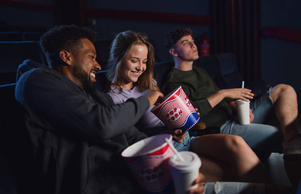 Cheerful young couple with popcorn in the cinema, talking. - 写真・画像