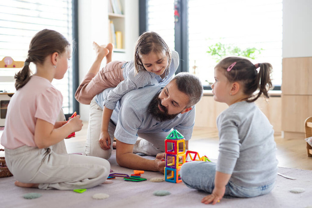 Father with three daughters indoors at home, playing on floor. - Photo, image