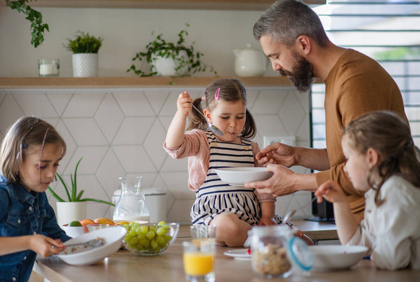 Father with three daughters indoors at home, eating breakfast in kitchen. - 写真・画像