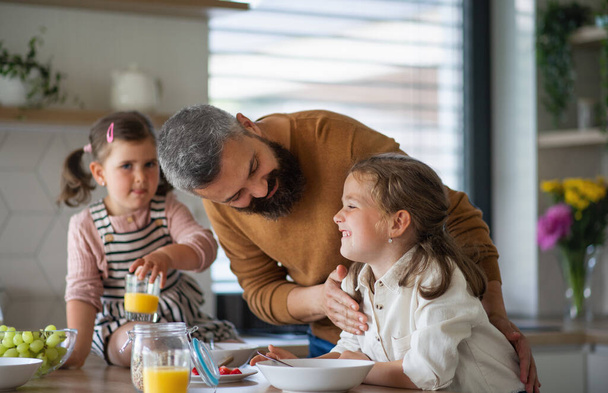 Father with three daughters indoors at home, eating breakfast in kitchen. - Fotografie, Obrázek