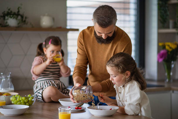 Father with three daughters indoors at home, eating breakfast in kitchen. - Foto, imagen