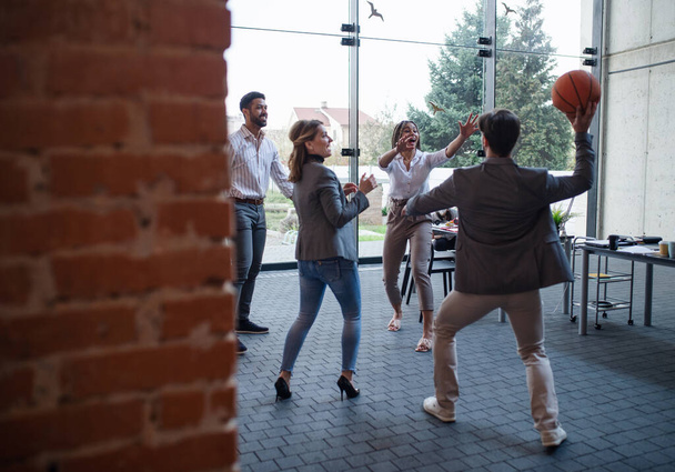 Group of cheerful young businesspeople playing basketball in office, taking a break concept. - Photo, image