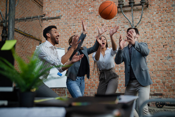 Bir grup neşeli genç iş adamı ofiste basketbol oynuyor, mola veriyorlar.. - Fotoğraf, Görsel