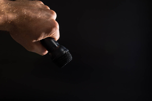 Czarny mikrofon w męskiej dłoni z przestrzenią do kopiowania, na czarnym tle. - Zdjęcie, obraz