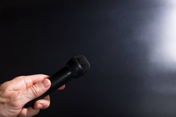 Mano maschile in possesso di microfono nero e prendere intervista su sfondo nero con spazio di copia. - Foto, immagini