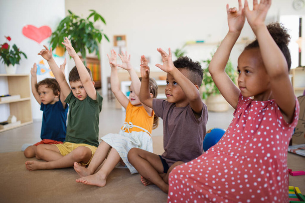 Gruppe von kleinen Vorschulkindern, die drinnen im Klassenzimmer auf dem Boden sitzen und spielen. - Foto, Bild