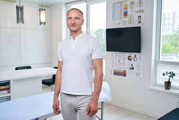 Przystojny umięśniony lekarz w białej koszuli stojący w gabinecie lekarskim - Zdjęcie, obraz