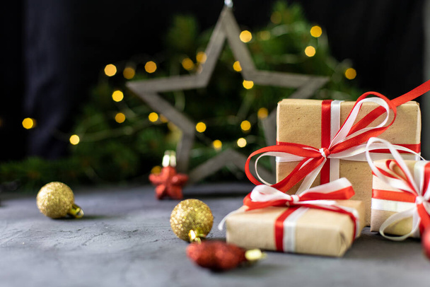 Cadeau de Noël en papier artisanal avec ruban blanc et rouge et sapin de Noël sur fond sombre avec étoile et bokeh doré. Joyeux Noël et bonne année. - Photo, image