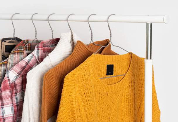Autumn vintage clothing hangs on hangers on the rack. Beige trench coat, sweaters, plaid shirts. Organization of space, winter cleaning. Mockup, template. - Photo, Image