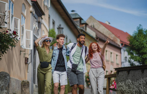 Front view of group of happy young people outdoors on trip in town, walking arm in arm. - Foto, Bild