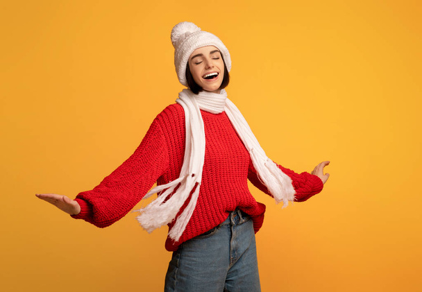 白いニットの冬のセットと赤いセーターのダンスでケアフリー遊び心のある女性と黄色の背景に回って - 写真・画像