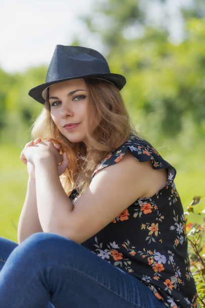 Cool young woman in straw hat is posing outdoors looking at the camera. Vertically.  - Foto, Imagen