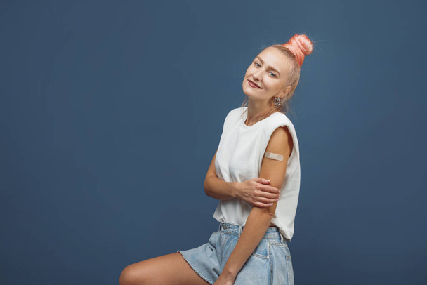 Young hipster woman with band aid after coronavirus Covid-19 vaccine injection. Covid vaccination concept, plain color background - Foto, Bild