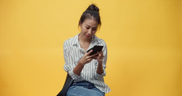 Happy beauty Asia youth casual girl smile enjoy typing smartphone message with friends stand over isolate yellow empty space background., Hands device chat online advertise. Face expression concept. - Footage, Video