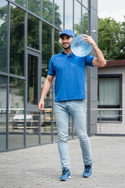 Cheerful muslim courier in uniform holding bottle of water outdoors  - Fotoğraf, Görsel