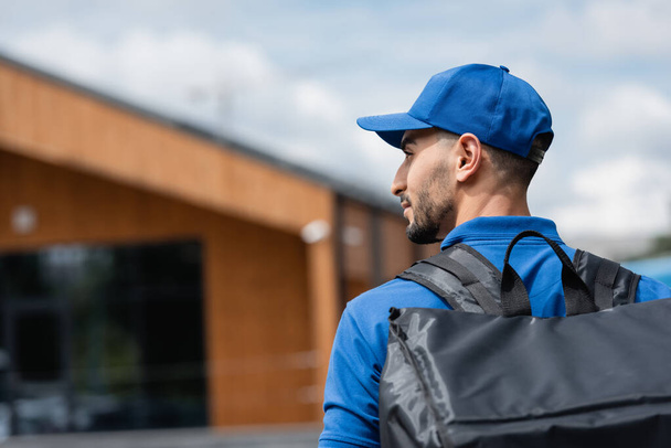 Side view of muslim deliveryman in uniform with thermo backpack outdoors  - Foto, Bild