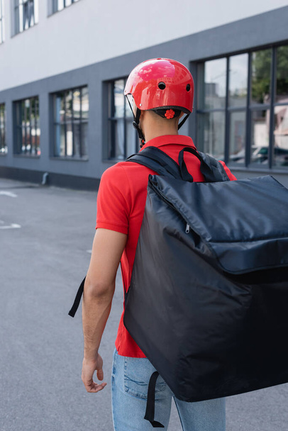 Back view of courier in helmet and thermo backpack standing outdoors  - Foto, imagen