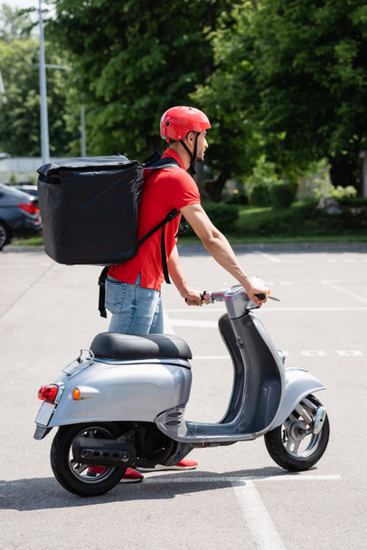 Side view of muslim deliveryman with thermo backpack standing near scooter  - 写真・画像