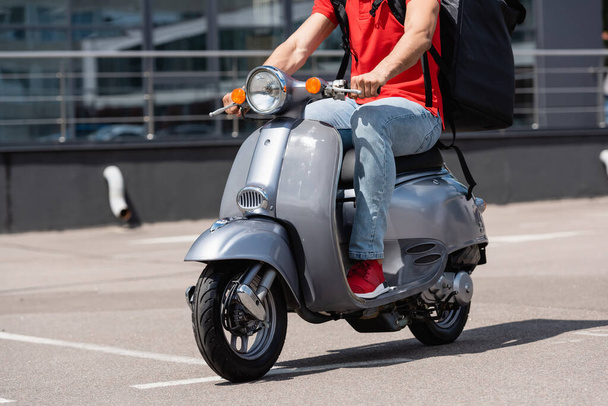 Cropped view of deliveryman in red t-shirt and thermo backpack driving scooter  - Φωτογραφία, εικόνα