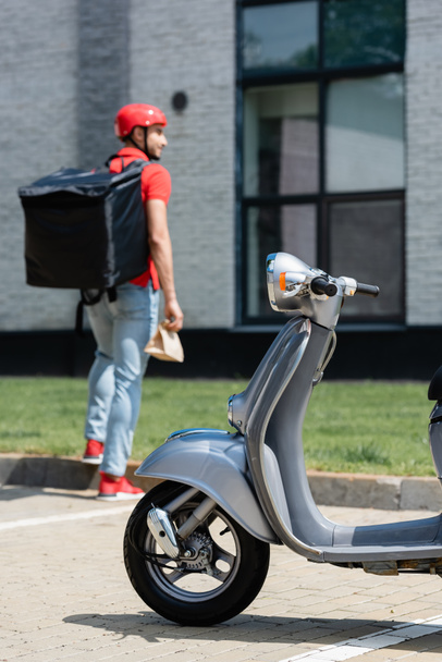 Scooter near blurred courier with thermo backpack and paper bag outdoors  - Fotoğraf, Görsel