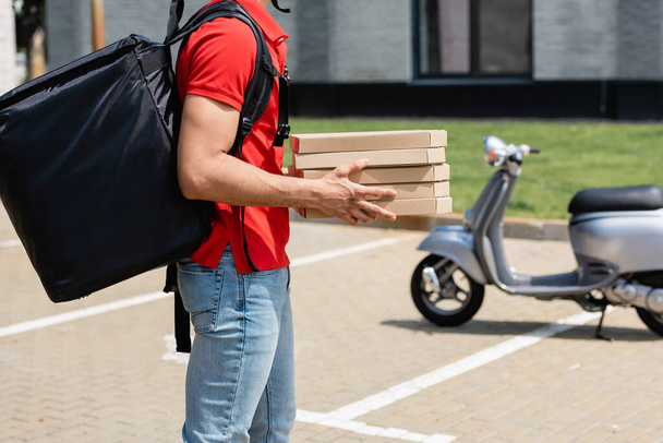 Cropped view of courier with thermo backpack holding boxes with pizza near blurred scooter outdoors  - Foto, Imagem