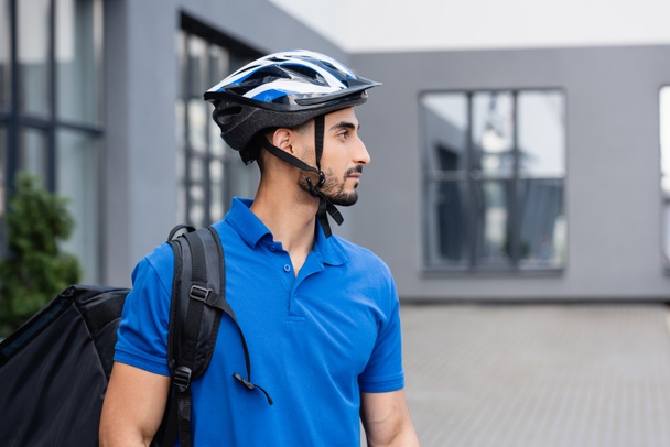 Side view of arabian courier in protective helmet with backpack outdoors  - Φωτογραφία, εικόνα