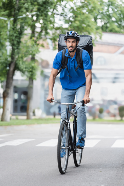 Muslim courier with backpack riding bicycle on urban street  - Photo, Image
