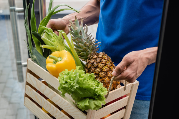 Gekropte blik op koeriersbox met biologische groenten en ananas bij de deur  - Foto, afbeelding