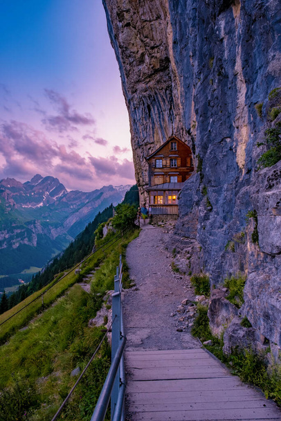 Swiss Alps and a mountain restaurant under the Aescher cliff viewed from mountain Ebenalp in the Appenzell region in Switzerland Aescher cliff - Photo, Image
