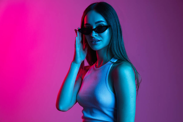 Beautiful young girl wearing sunglasses isolated on gradient pink purple background - Fotó, kép