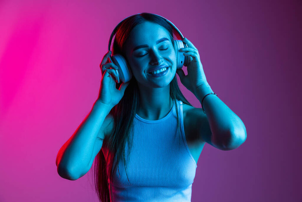 Cropped close-up portrait of young beautiful smiling girl wearing headphones and listening to music - Foto, Imagen