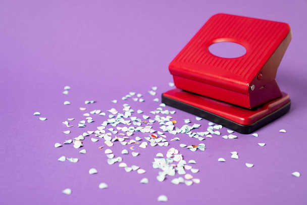 Red hole punch with a lot of paper confetti. White paper confetti from red hole puncher on violet background - Photo, Image