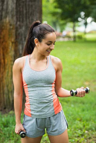 smiling young sportswoman exercising with dumbbells in park - Foto, Imagem
