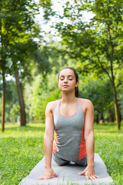 giovane donna con gli occhi chiusi meditando sul tappetino yoga nel parco  - Foto, immagini