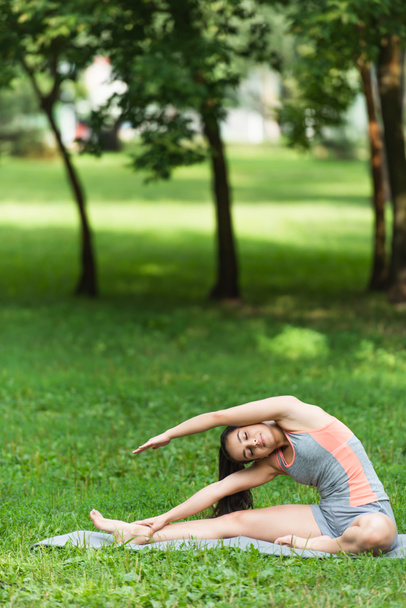 гнучка і підходить жінка в спортивному одязі, що тягнеться на йога мат в парку
 - Фото, зображення