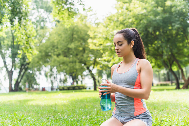 young fit woman holding sports bottle with water in park - Foto, afbeelding