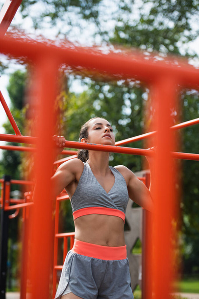 junge Frau trainiert auf verschwommenem Pull-up-Stab in Outdoor-Fitnessstudio  - Foto, Bild