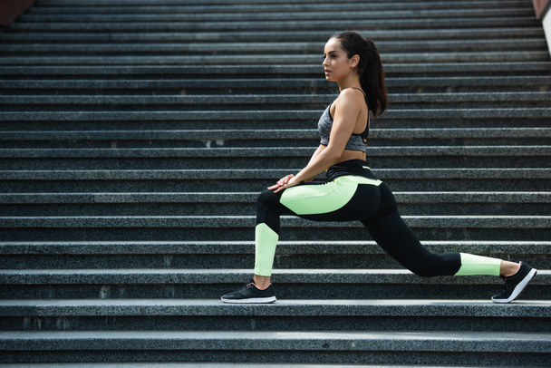 full length of sportive woman doing lunge on stairs outside  - 写真・画像