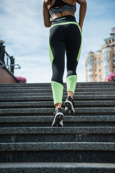 cropped view of sportive woman running on stairs outside  - Foto, Imagen