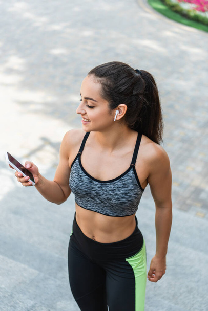 vista de ángulo alto de la deportista feliz en auriculares inalámbricos con teléfono inteligente con pantalla en blanco fuera  - Foto, Imagen